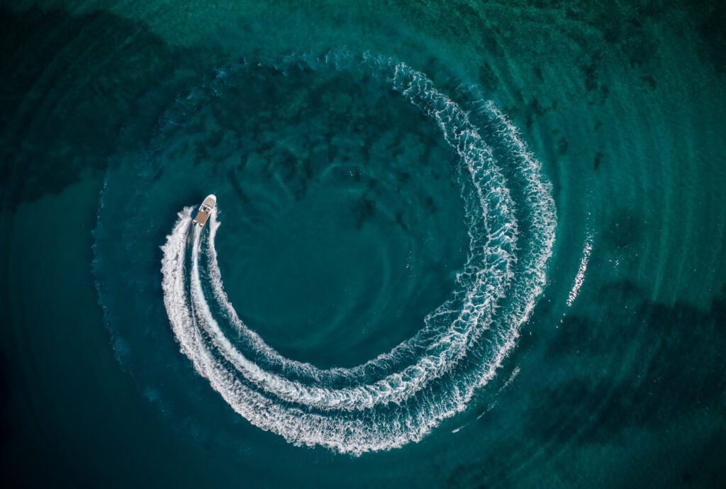 Aerial view of speed motor boat in shallow water, creating wheel shape.