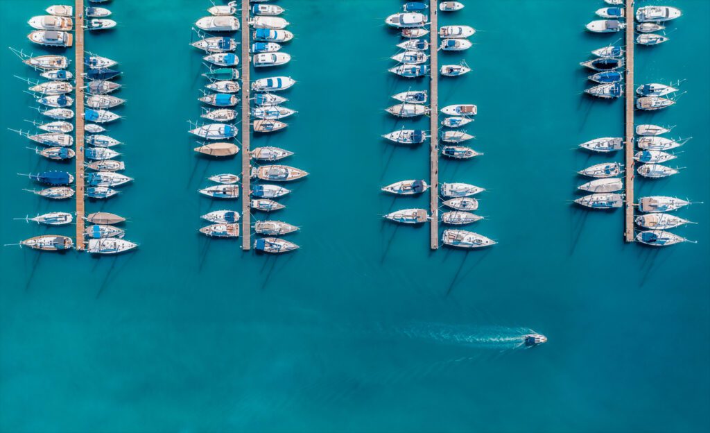 Aerial view of luxury yachts and motorboats moored in a port with clear blue water in summer. Top view from drone of sailboats and various speed boats in dock.